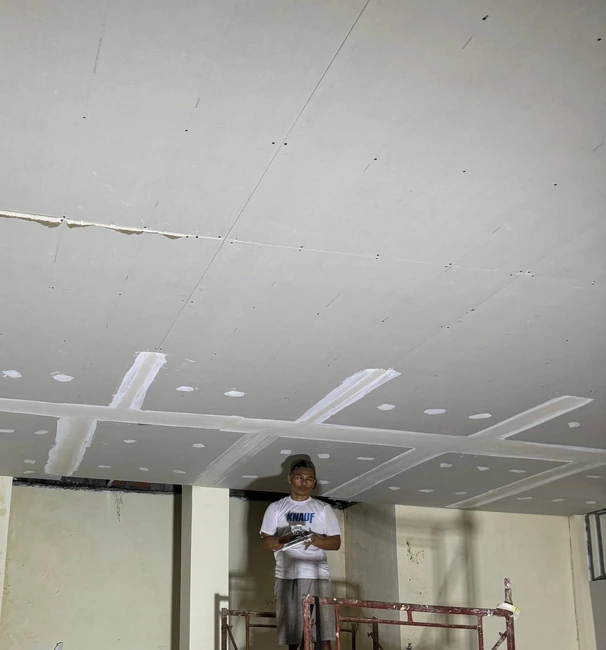 Pekerja di perancah di bawah plafon dengan pekerjaan finishing sambungan yang berlangsung.