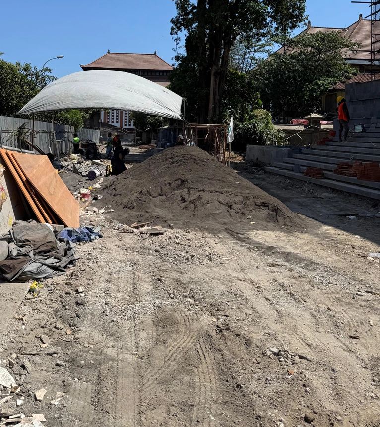 Kondisi lokasi konstruksi dengan penyimpanan material dan pekerja di dekat tangga pintu masuk.