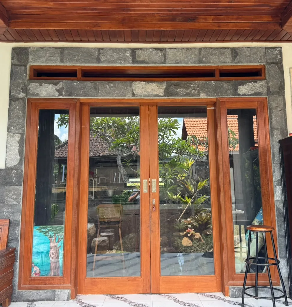 Installed timber-and-glass double door with glazed sidelights and an upper opening within the existing stone-finished wall.