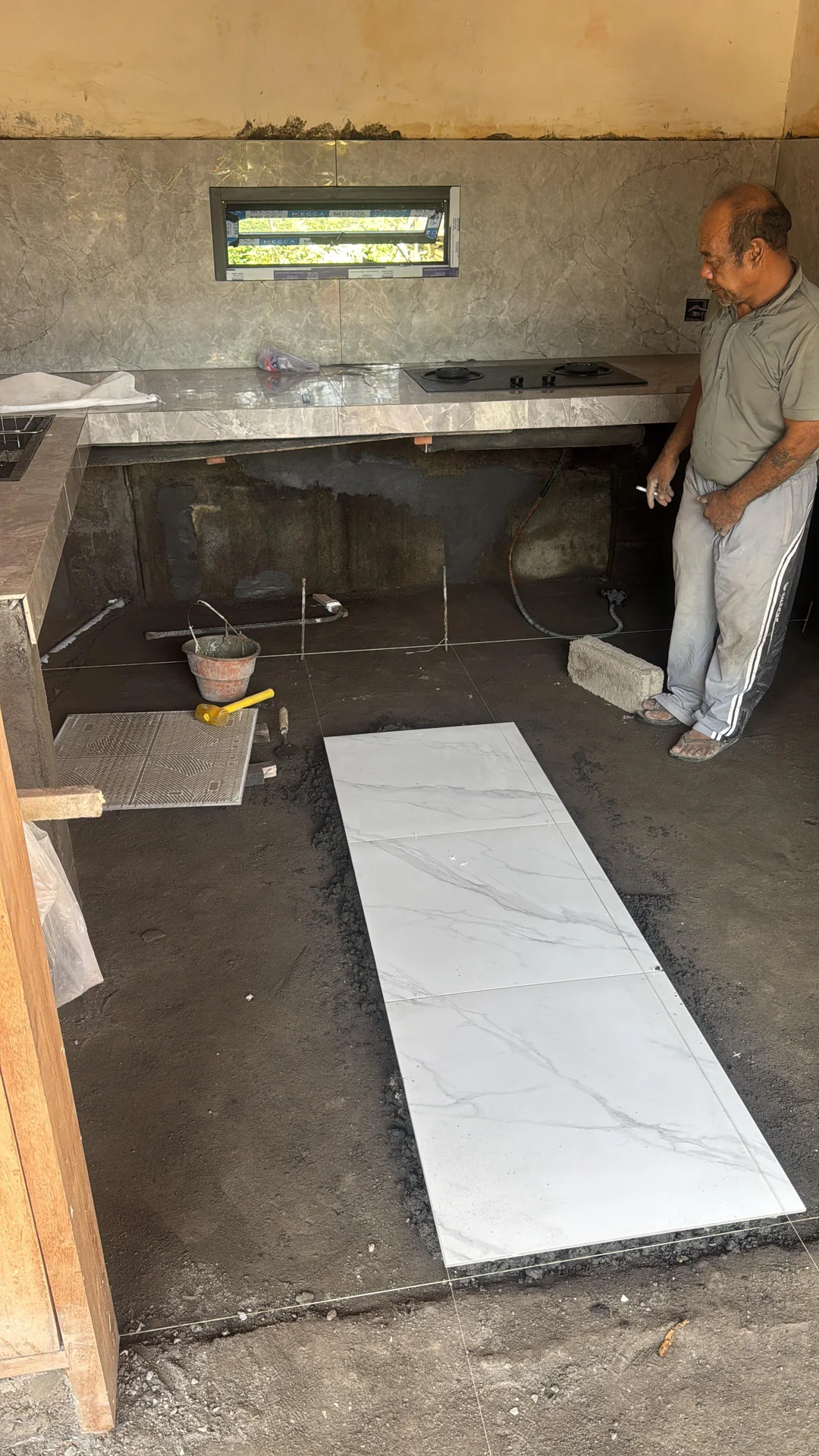 Stone-look kitchen counter above unfinished masonry bases while floor tiles are being laid.